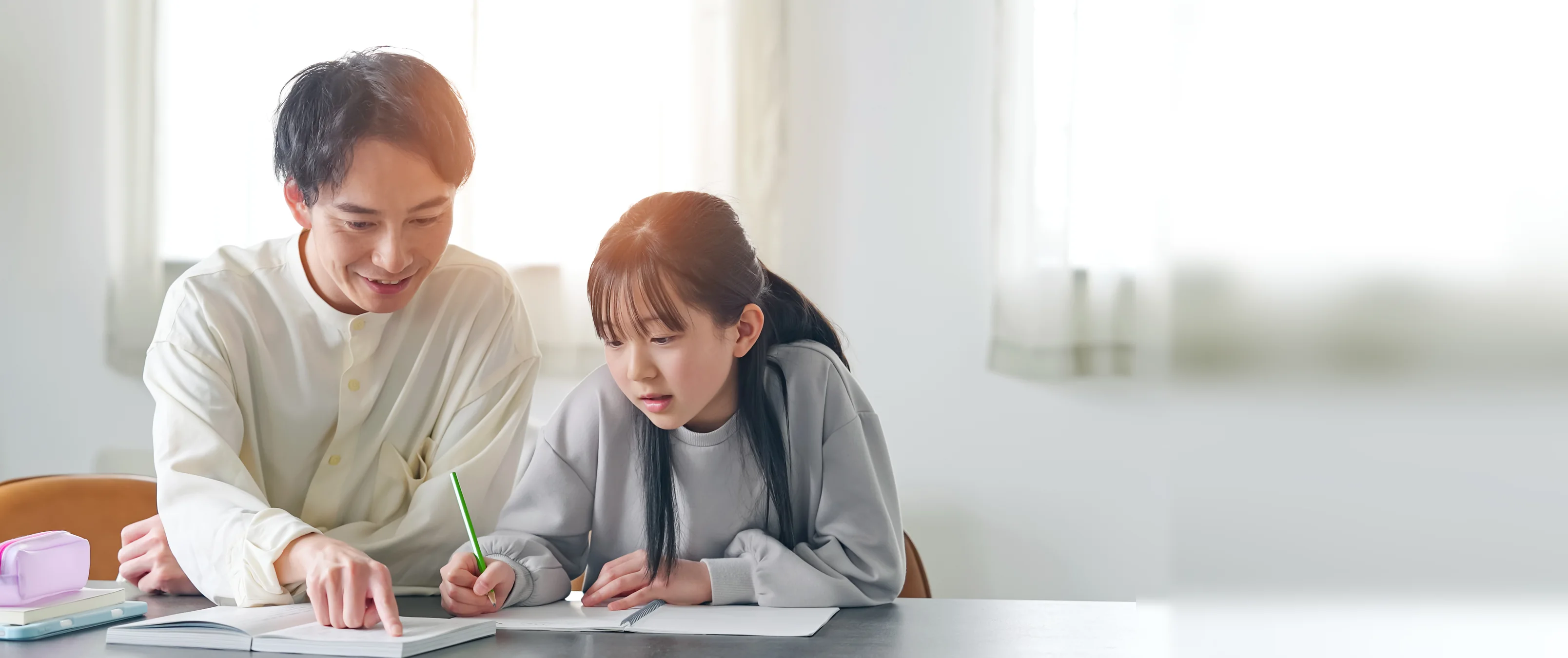 ノートを指しながら教える家庭教師と、集中して取り組むお子様。特性に合わせた1対1の学習サポート