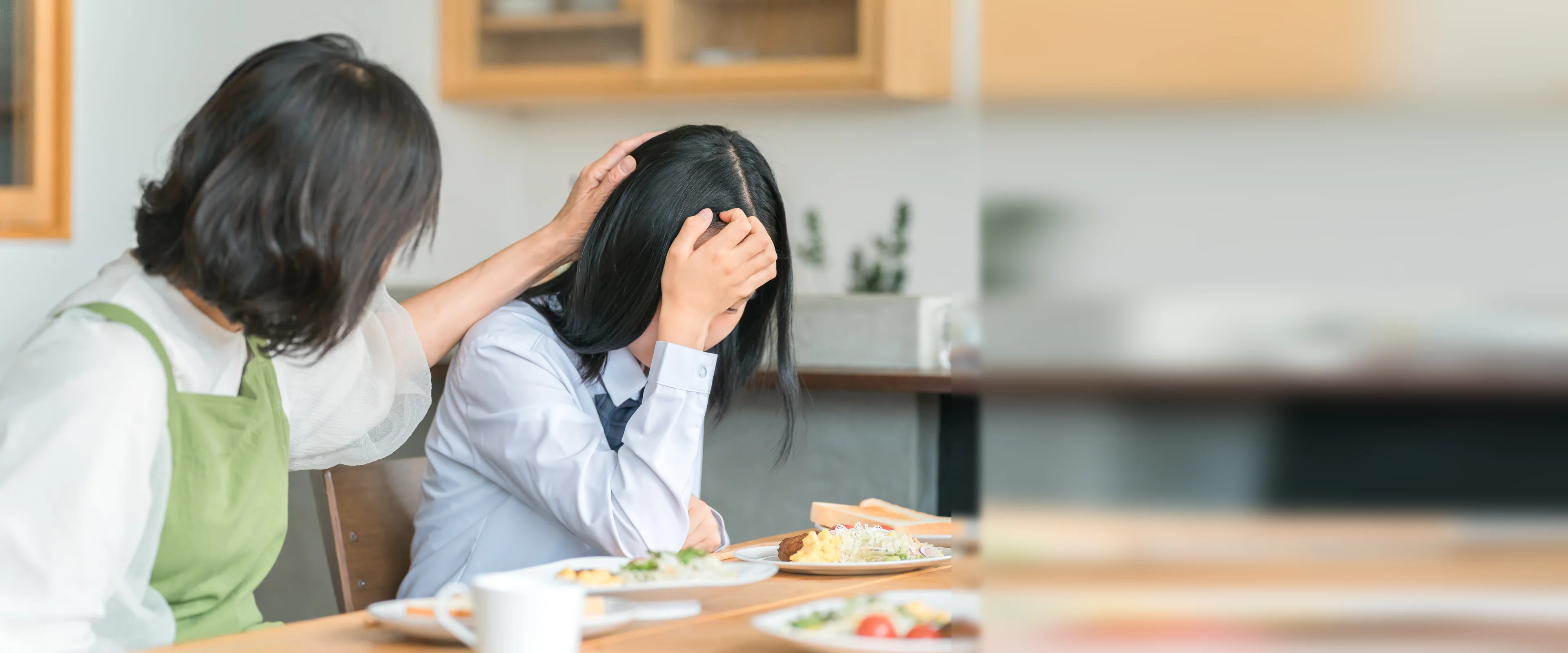 食卓でうつむくお子様に寄り添う保護者。不登校のお子様を家庭教師がご自宅で1対1でサポート